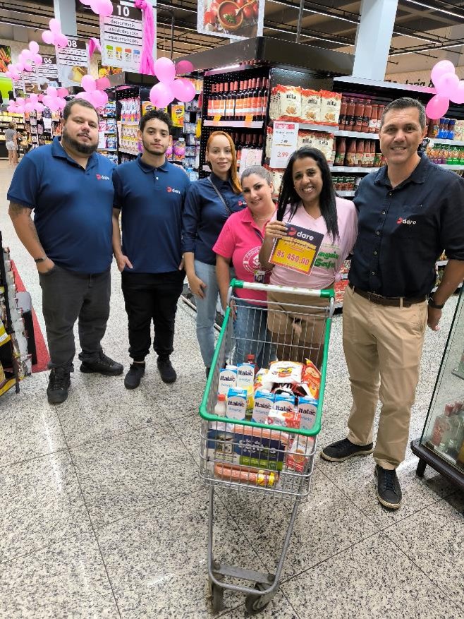 Equipe do Dia DARE e participantes do Projeto Caju ao lado de um carrinho com alimentos adquiridos com o vale-compras.