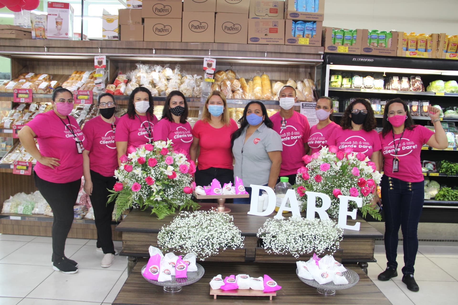 Equipe de supermercado com camisetas Dia DARE reunida em loja decorada para o evento.