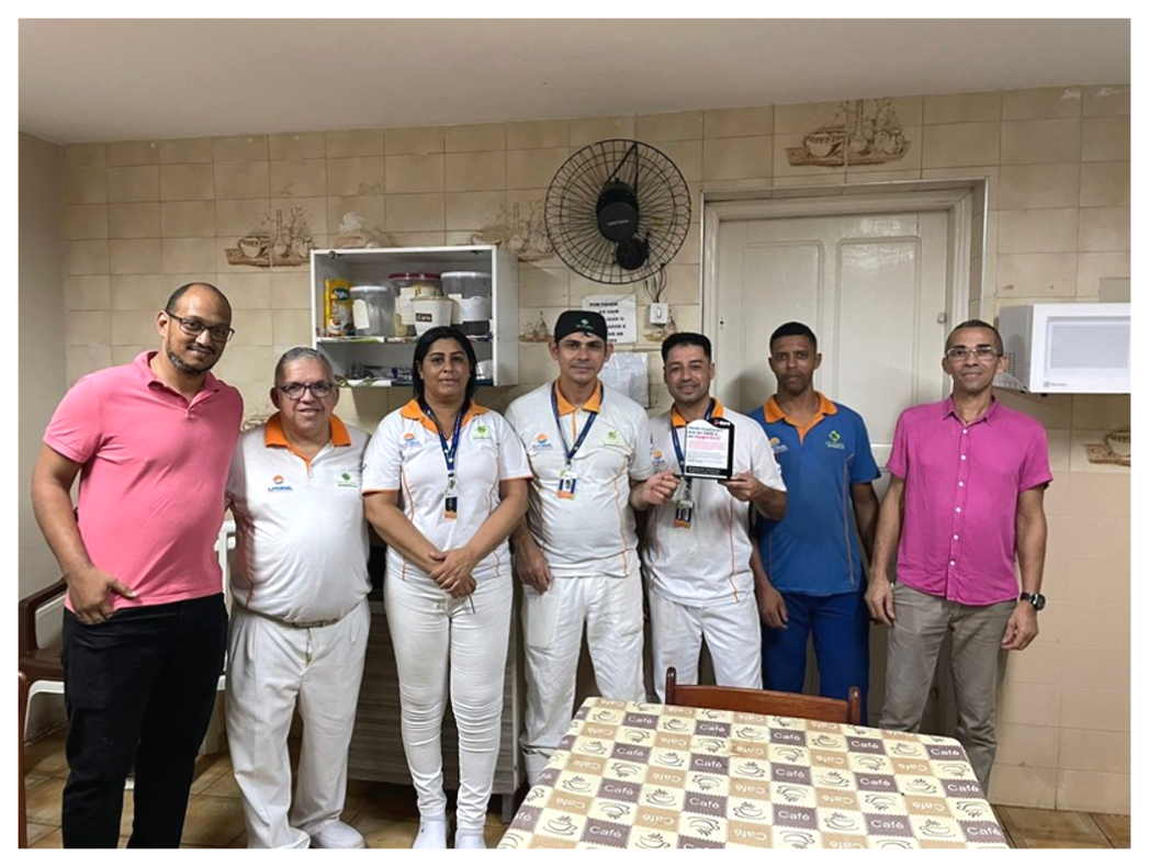 Equipe de supermercado com uniformes e camisas rosa Dia DARE reunida em copa, com placa de reconhecimento.